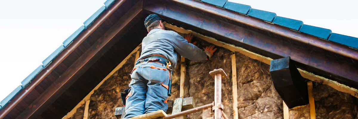 Construction worker thermally insulating house facade with glass