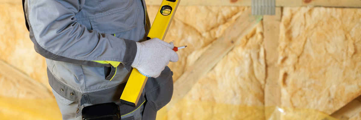 Construction mason worker with building level and screwdriver on attic with environmentally friendly and energy efficient thermal insulation rockwool.