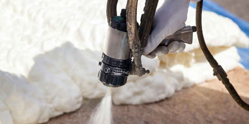 Technician spraying foam insulation using plural component spray gun