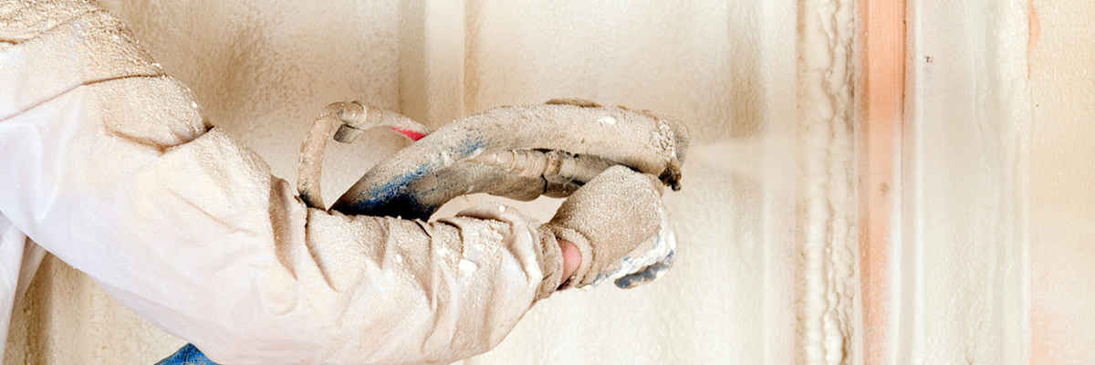 Construction worker spraying expandable foam insulation between wall studs