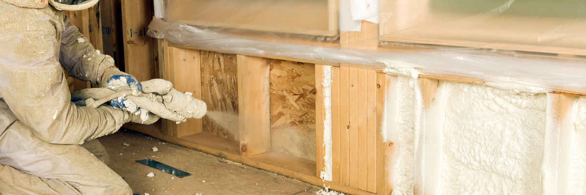 Construction worker spraying expandable foam insulation between wall studs